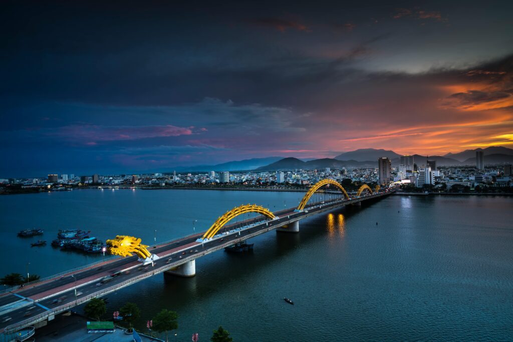 A stunning aerial view of the Dragon Bridge at sunset in Da Nang, Vietnam, highlighting illuminated cityscape.