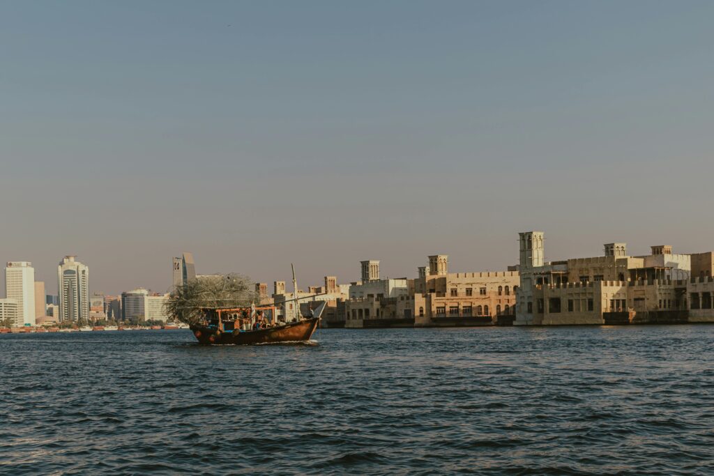 Traditional dhow sailing on Dubai Creek with a backdrop of historic architecture and modern skyscrapers.