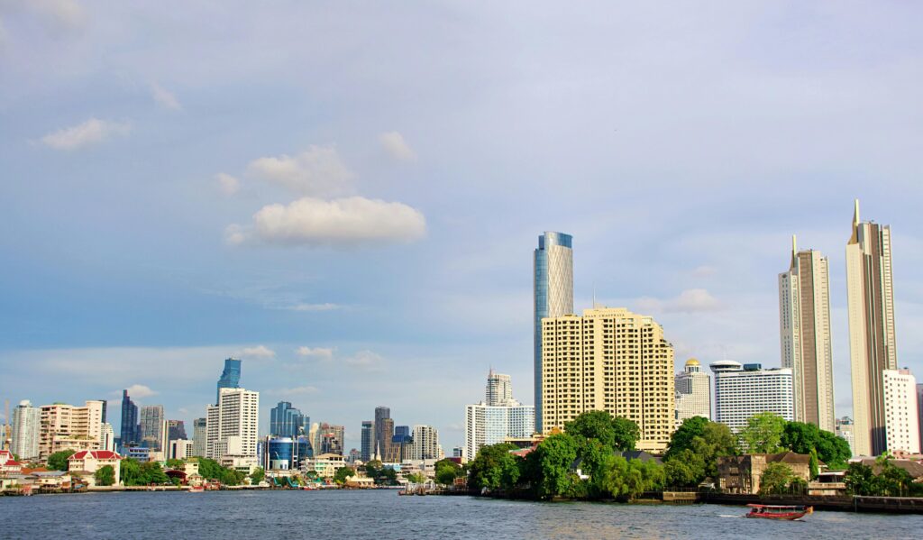 Modern Bangkok skyline along the Chao Phraya River under a clear blue sky.